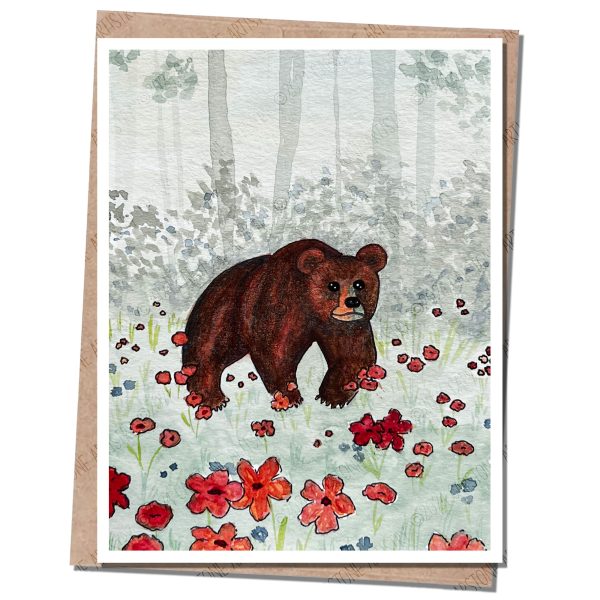 A bear in a field of flowers with trees and forest in the distance.